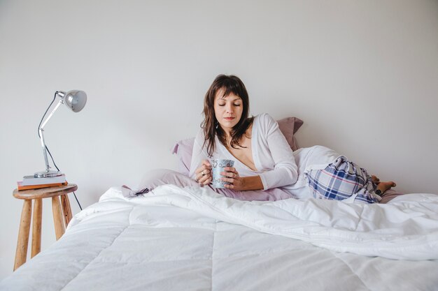 Woman on bed looking at her coffee