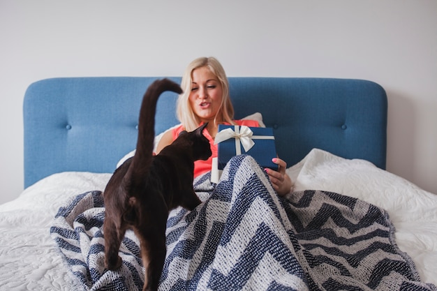 Free photo woman on the bed with a gift and a cat