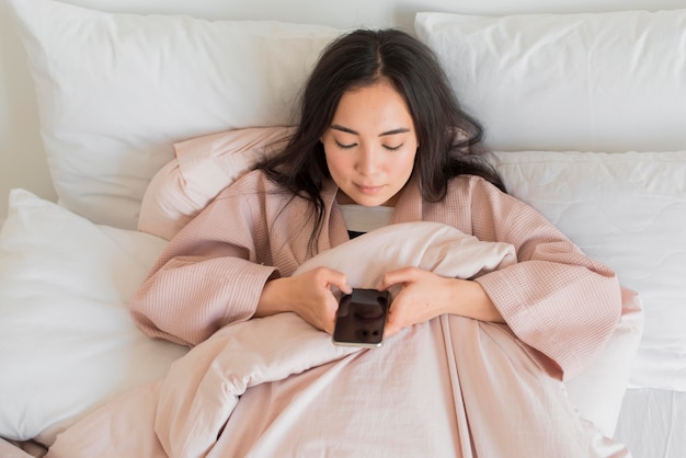 携帯電話でベッドの上の女性