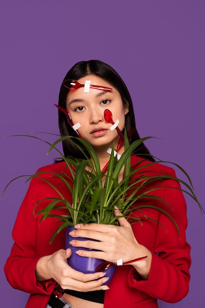 Woman being covered in plastic spoons and forks while holding a plant