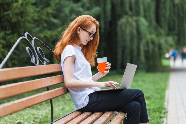 Woman on bench with laptop and juice 
