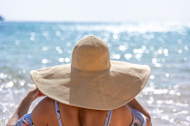 大きな帽子をかぶった女性が海の近くのビーチで日光浴をします。