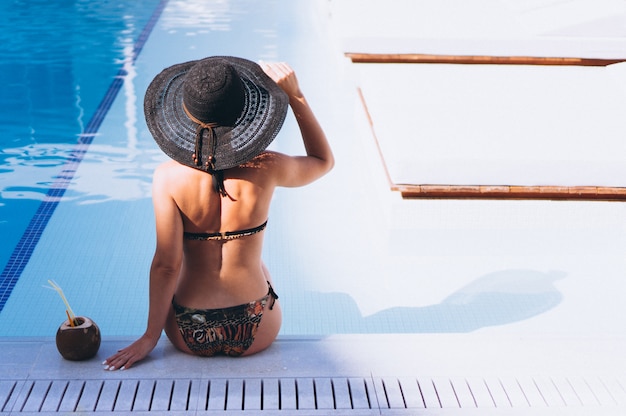 Free photo woman in bikini drinking coconut milk by the pool