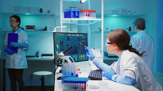 Woman biochemist checking manifestations of virus working on computer in equipped lab late at night