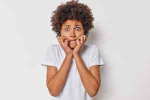 Free photo woman bites finger nails looks anxious at camera feels worried about something being in panic wears casual t shirt isolated on white being afraid of terrible thing