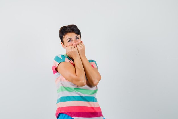 Woman biting fists emotionally in striped t-shirt and looking scared.