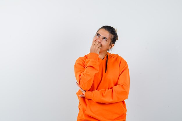 Woman biting her nails in orange hoodie and looking dreamy