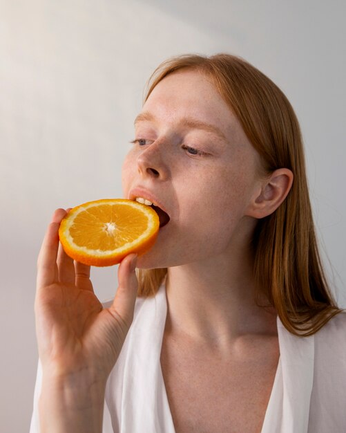 Женщина кусает дольку апельсина, вид сбоку