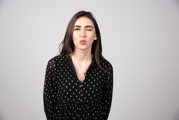 Woman in black dress giving kisses on gray.