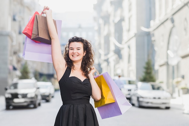 Woman in black dress raising her arms with colorful shopping bags