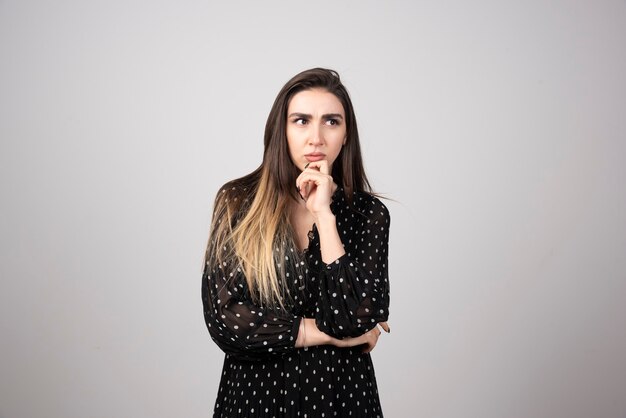 Woman in black dress thinking on gray.