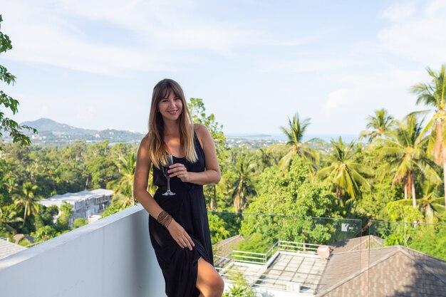 熱帯のバルコニーでワインのガラスと黒のイブニングドレスの女性