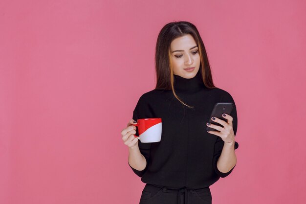 Woman in black shirt holding a coffee cup and talking to the phone. 