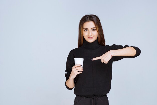 woman in black shirt holding a disposable coffee cup and promoting it.