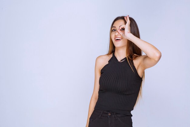 Woman in black shirt looking through her fingers. 