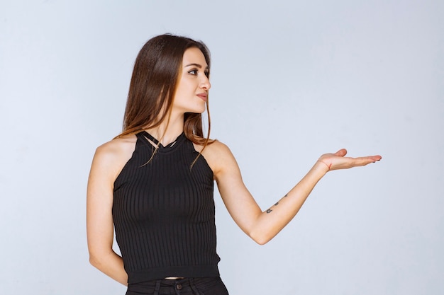 Woman in black shirt opening hand and holding or presenting something. 