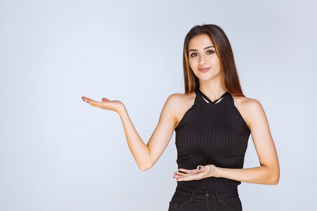 Free photo woman in black shirt opening hand and holding or presenting something.