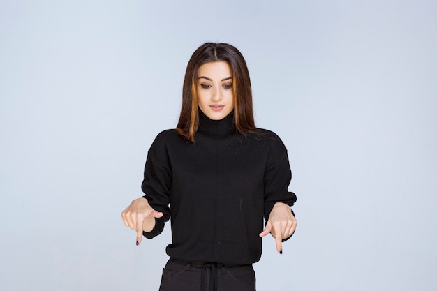 woman in black shirt pointing at downside. 