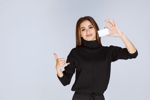 woman in black shirt showing her business card and looks satisfied. 