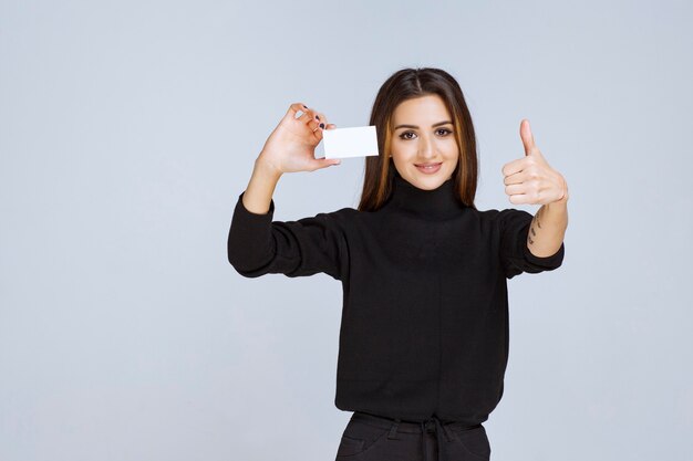 woman in black shirt showing her business card and looks satisfied. 