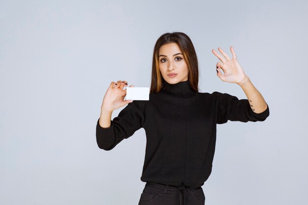 woman in black shirt showing her business card and looks satisfied. 