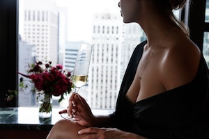 Woman in black silk robe with opne shoulders and breast holds glass with champagne