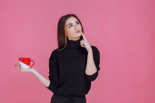 Donna in maglione nero che mangia caffè e pensa.