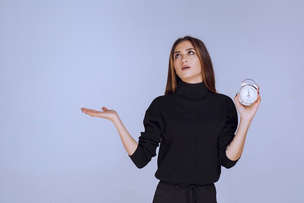 Free photo woman in black sweater holding the alarm clock and promoting it.