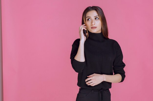 Woman in black sweater holding a smartphone to ear and talking. 