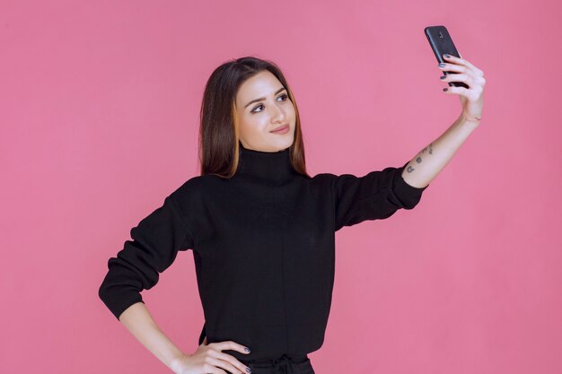 スマートフォンを持って自分撮りをしている黒いセーターの女性。
