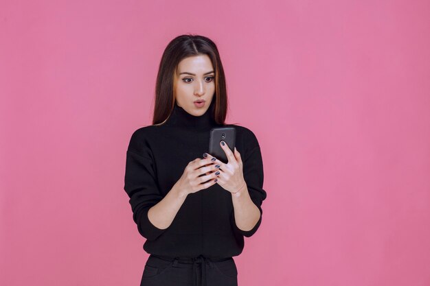 Woman in black sweater holding a smartphone and texting or checking social media. 