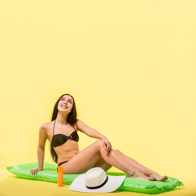 Woman in black swimsuit sitting on water mattress and smiling