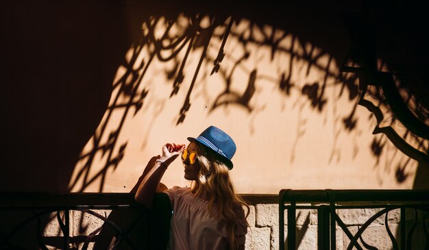 Woman in blue hat poses before a wall with shadows 