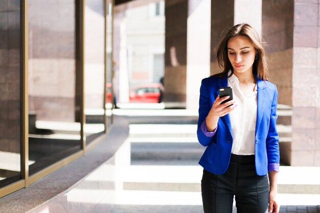 青いジャケットの女性は彼女の電話をチェックします