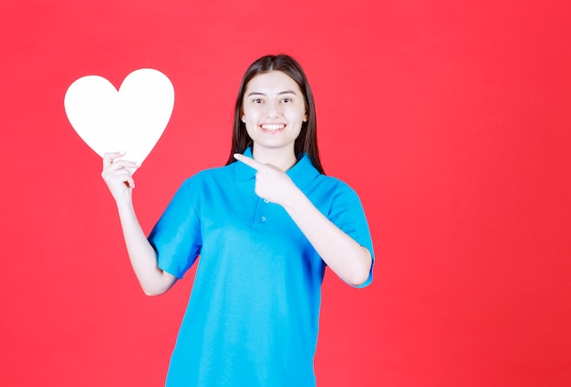 Foto gratuita donna in camicia blu che tiene un pannello informativo a forma di cuore.