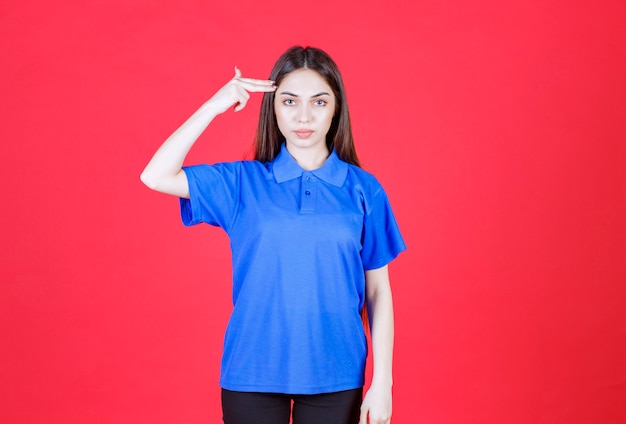 赤い壁に立っている青いシャツを着た女性は、混乱して思慮深く見えます。