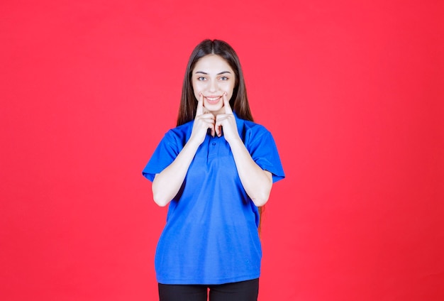 Donna in camicia blu in piedi sul muro rosso.