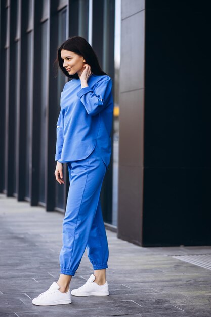 Женщина в синей спортивной одежде стоит снаружи у здания