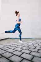 Foto gratuita donna in abiti sportivi blu che salta sulla strada