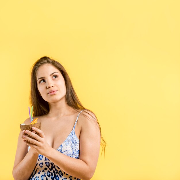 Woman in blue swimsuit standing and holding coconut drink in hands