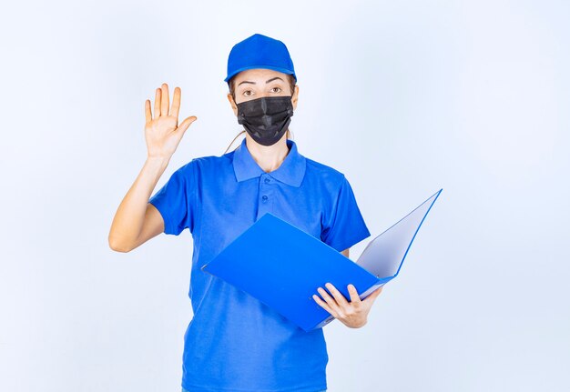 青い制服と黒いフェイスマスクの女性がレポートをチェックし、間違いに注意を向けています。