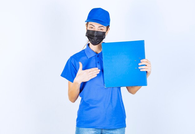 Donna in uniforme blu e maschera nera con in mano una cartella dei rapporti blu.