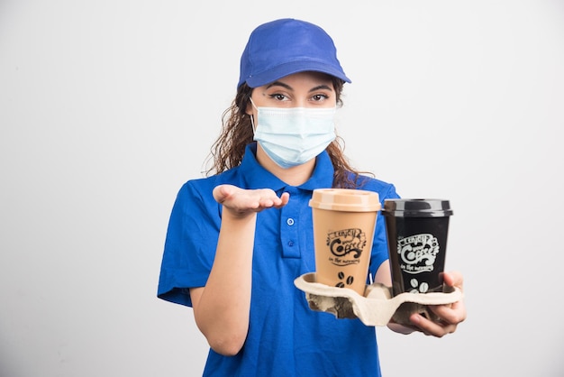 Woman in blue uniform with medical mask holding two cups of coffee on white