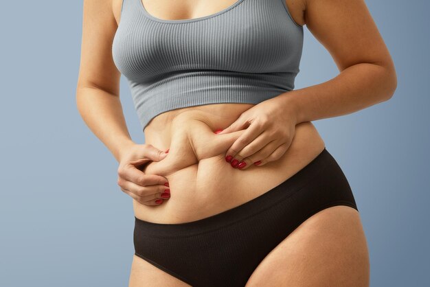 過剰なおなか脂肪を保持している女性の体脂肪腹肥満女性の手は、健康的な胃の筋肉スタジオを形作るためにダイエットライフスタイルの概念を変更します体の部分の匿名のショット写真