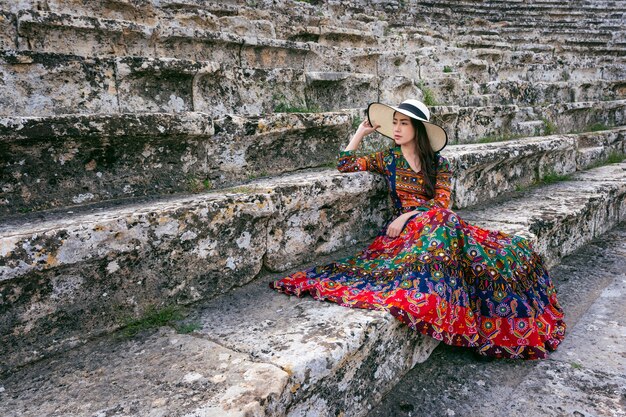 Женщина в богемном платье сидит на театре древнего города Иераполис в Памуккале, Турция.