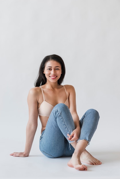 Woman in bra and denim sitting on floor