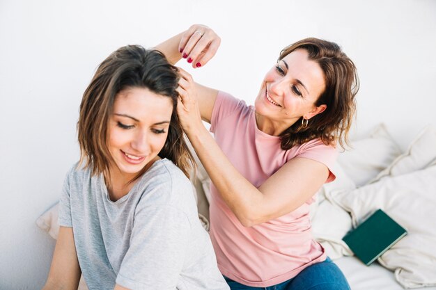 Woman braiding hair of woman on sofa