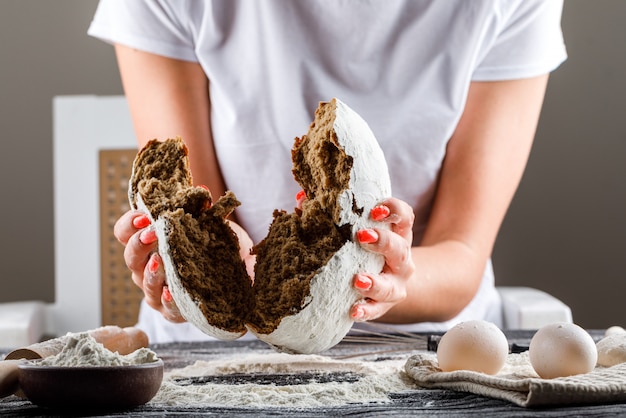 Torta frenante della donna a metà con il perno delle uova, farina su una vista laterale della tavola di legno scura