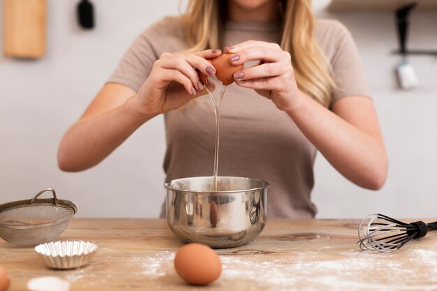 Женщина разбивает яйца в металлической миске