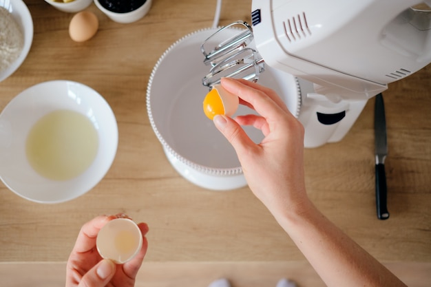 Woman breaks chicken eggs in a bowl in the kitchen.